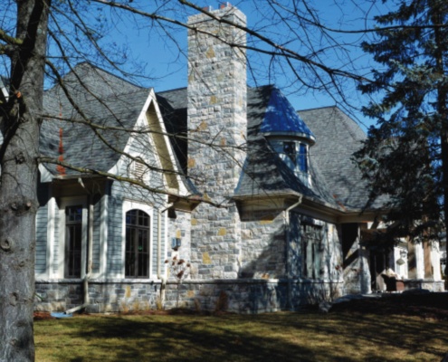 Traditional house with blue siding, stone chimney, and stone skirt.