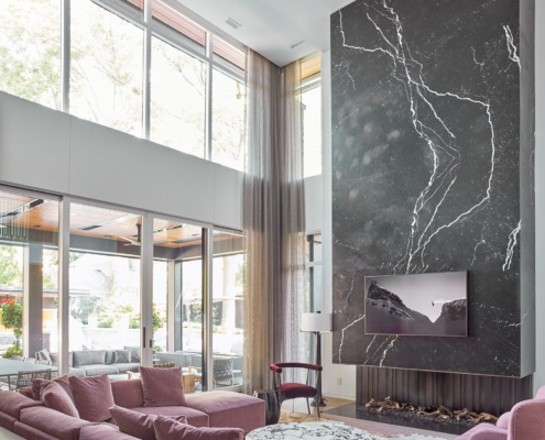 Living room with vaulted ceilings, marble fireplace and white frame windows.