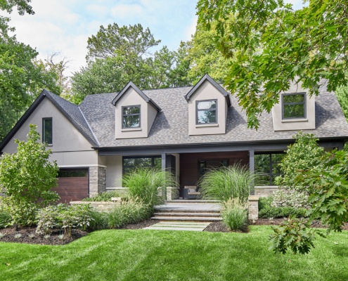 Custom home with black frame window, shingled roof and wood garage door.