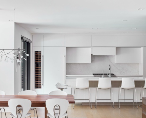Modern dining room and kitchen with white trim, white walls and hardwood floor.