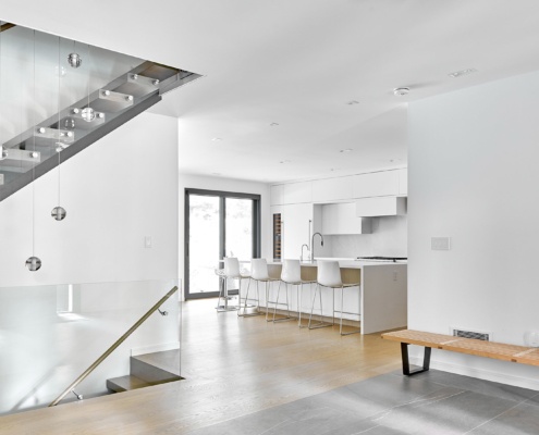 Modern kitchen with white island, white cabinetry and floating staircase.