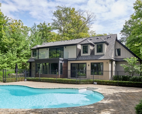 Transitional home with stucco siding, black frame windows and inground pool.