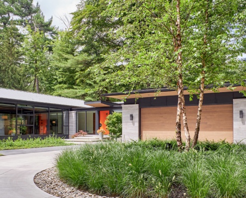 Mid century modern house with metal roof, wall sconce and concrete driveway.