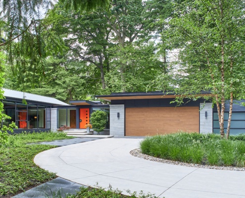 Bungalow with orange door, wood garage door and metal cladding.