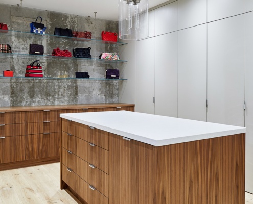 Walk in closet with chandelier, concrete wall and white cabinets.