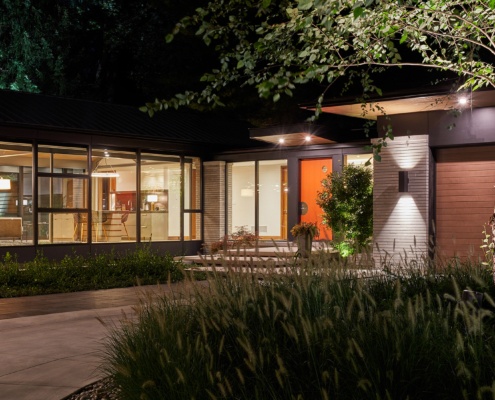 Bungalow at night with orange front door and wall sconce.