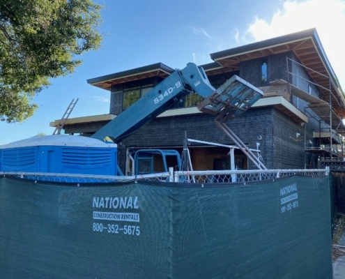 Natural modern home in construction with flat roof, black frame windows and black trim.