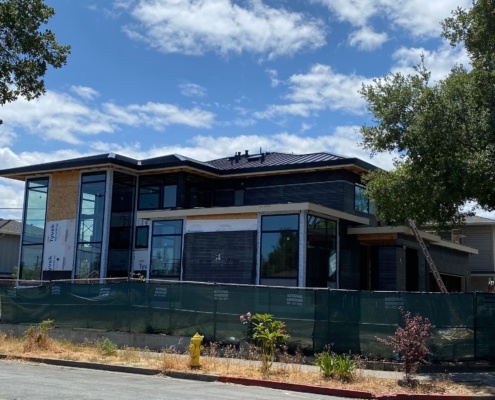 Modern home in construction with floor to ceiling windows and metal roof.