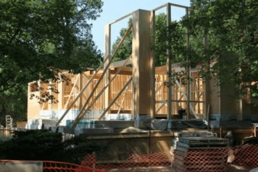 An under-construction house with visible wooden framing, enclosed by bright orange fencing for safety.