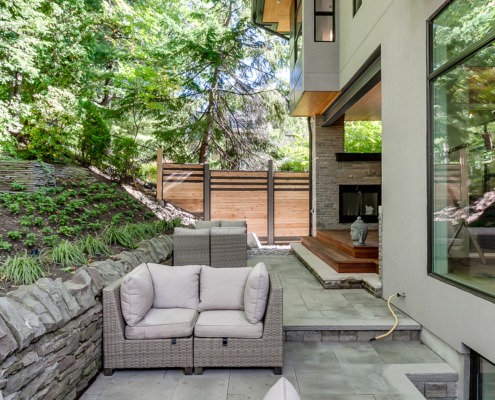 House backyard with stone retaining wall, flagstone patio and black frame window.