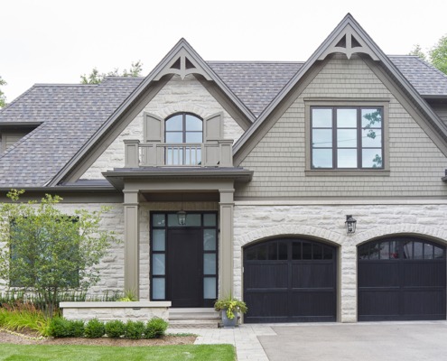 Oakville house with dark garage door, shingled roof and green trim.