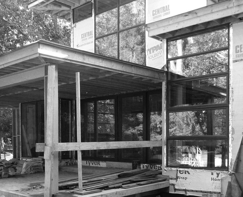 Home in construction with corner windows, natural stone and black cladding.