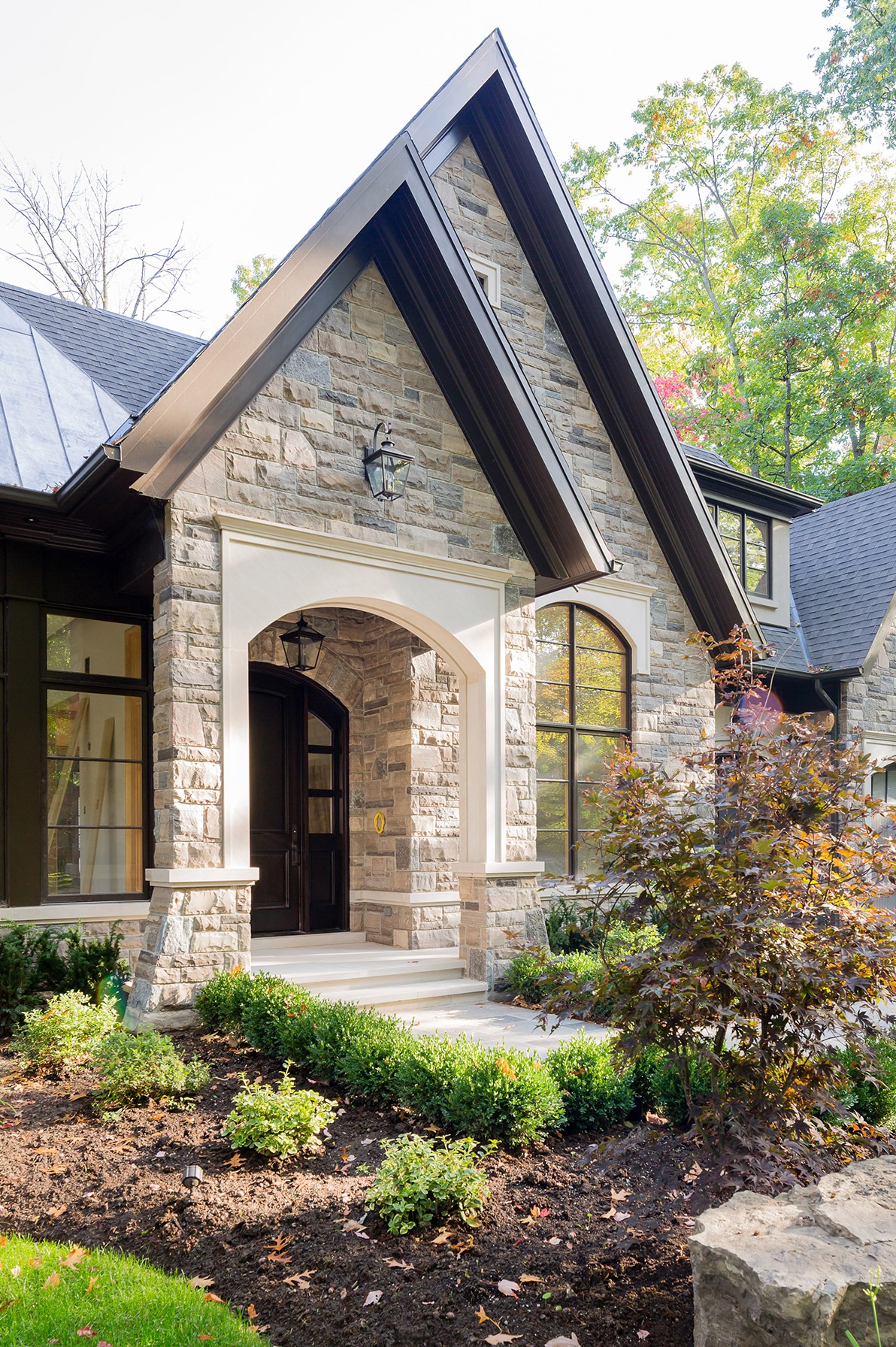 Traditional home front entry with angled stone, wood door and black frame windows.