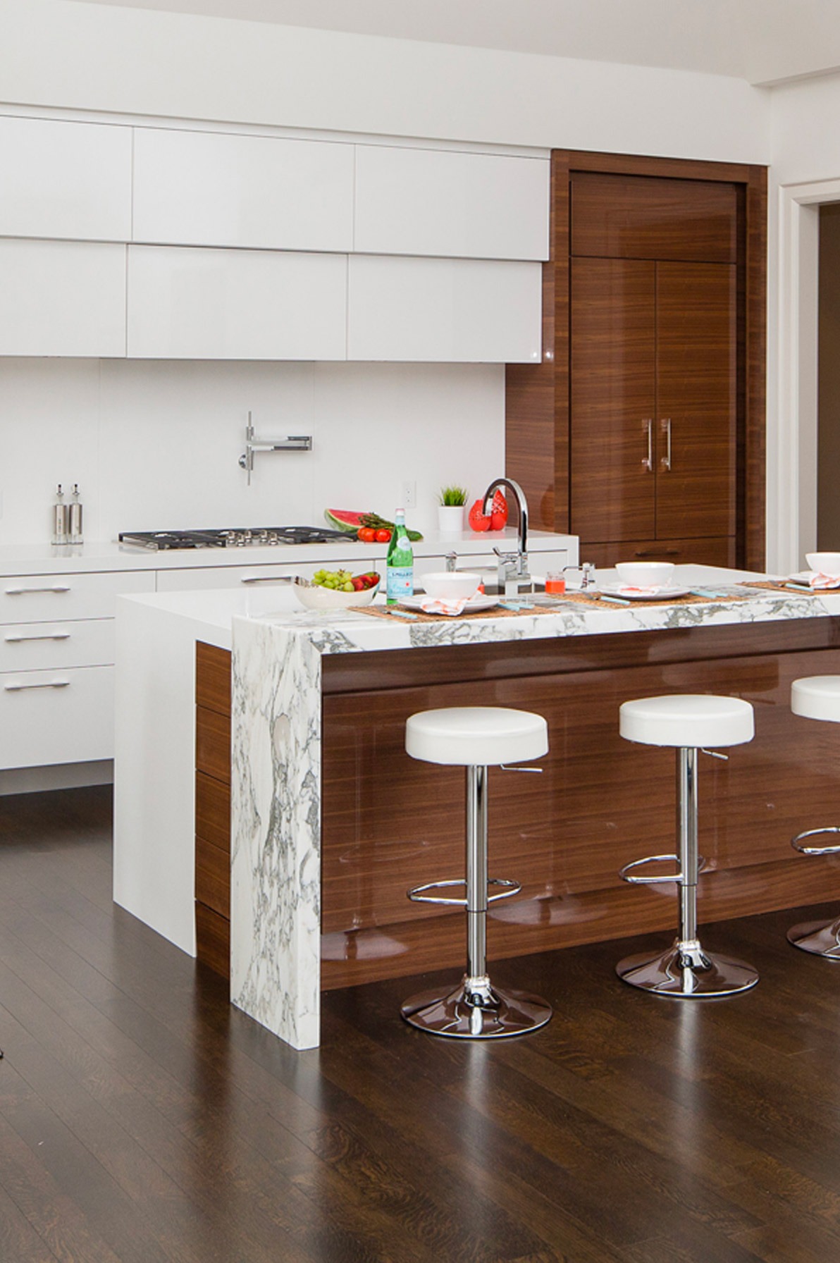 White kitchen with wood cabinets, white backsplash and marble countertop.