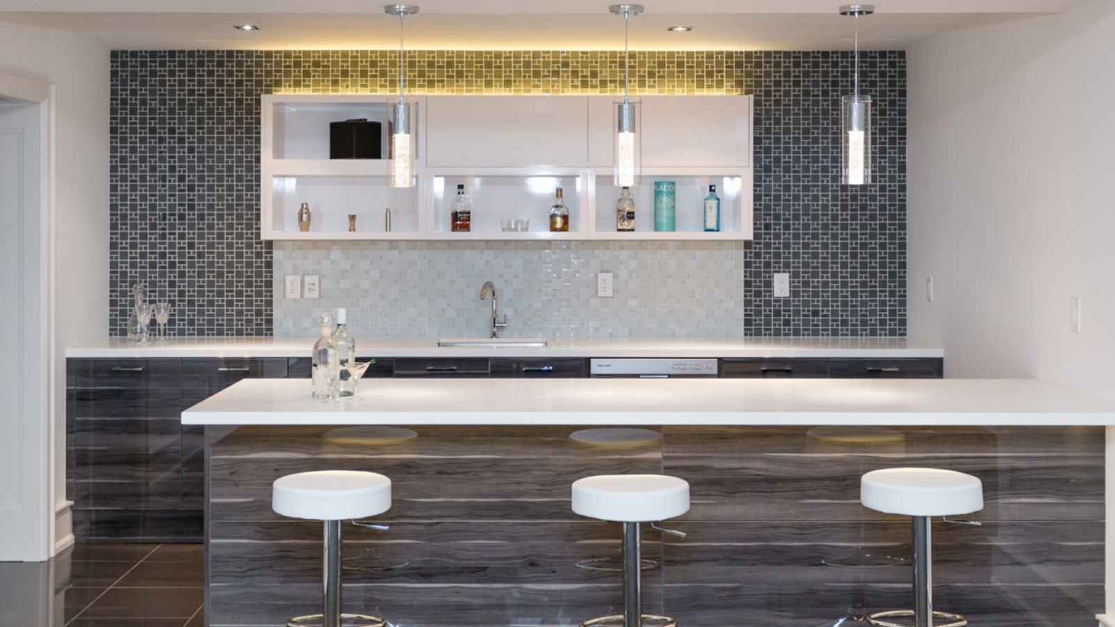 Home bar with white countertop, tile backsplash and white barstools.