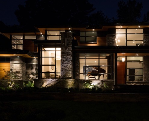 Mississauga home at night with black frame windows, wood siding and natural stone.