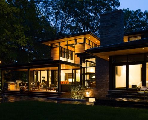 Modern home at night with floor to ceiling windows, wood siding and floating roof.