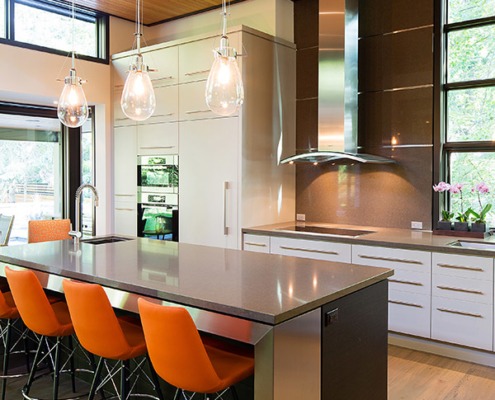 Modern kitchen with large island, white drawers, hardwood floor and range hood.