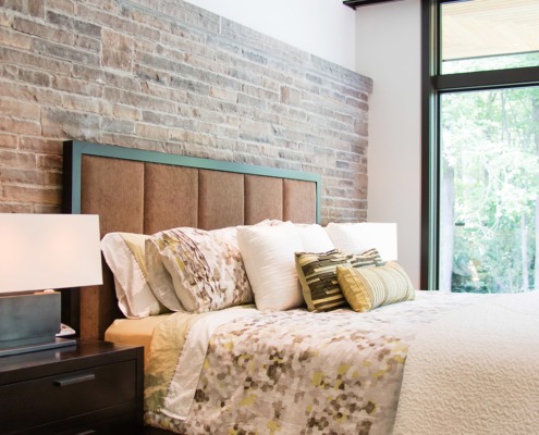 Master bedroom with stone wall, floor to ceiling windows and wood nightstand.