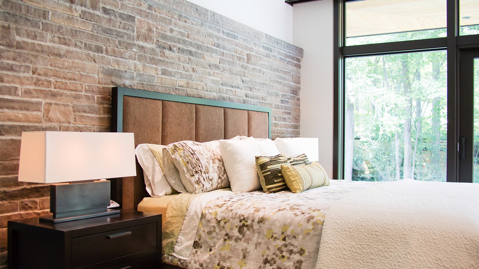 Master bedroom with stone wall, floor to ceiling windows and wood nightstand.