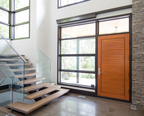 Home front entry with wood door, black frame windows and floating staircase.