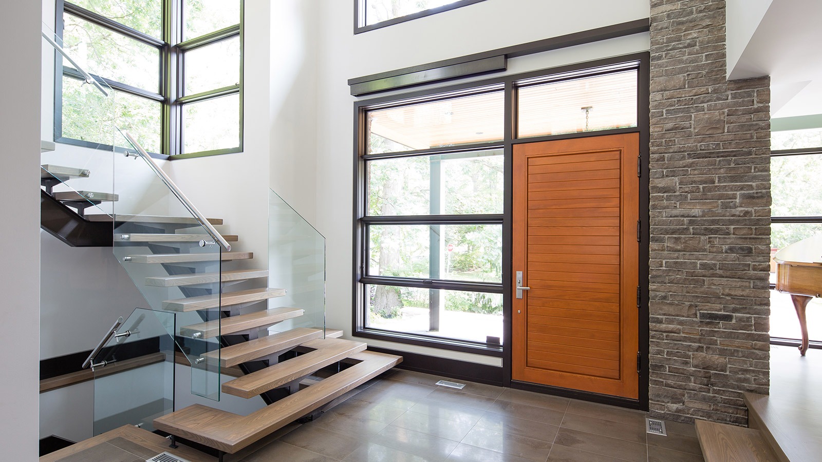 Home front entry with wood door, black frame windows and floating staircase.