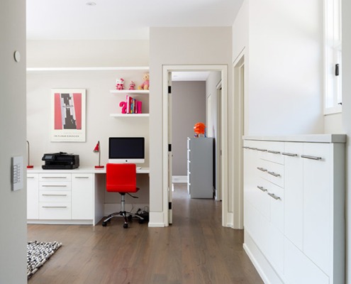 Work studio with hardwood floor, built in desk and white baseboard.