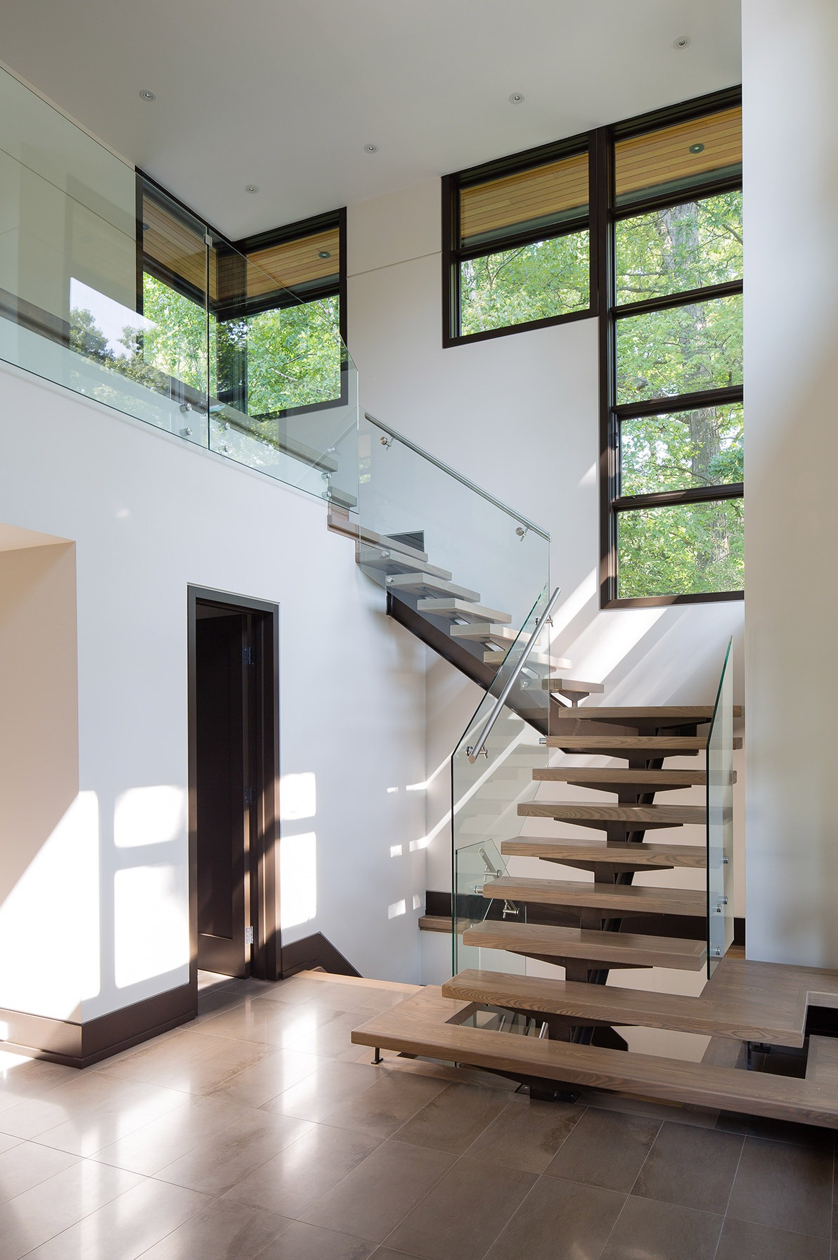 Modern floating stair with wood treads, tile floor and black baseboard.