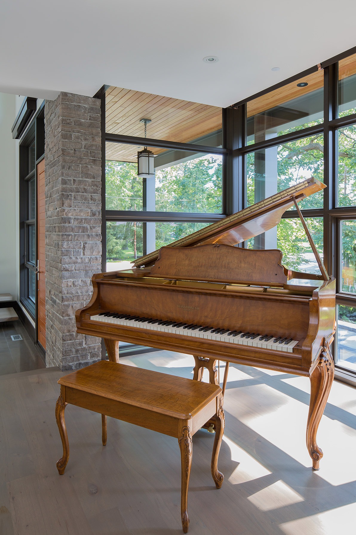 Modern home with grand piano, exposed stone and black frame windows.