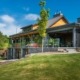 Cottage with stone chimney, glass railing and wood soffit.