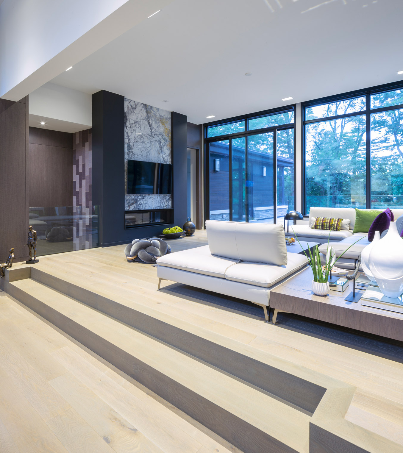 Living room with hardwood floor, marble fireplace and black frame window.