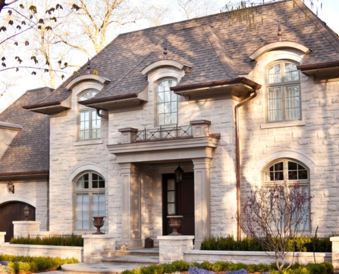 Chateau style home with light stone, wood front door and arched window.