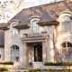 Chateau style home with light stone, wood front door and arched window.
