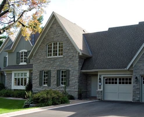 Traditional home design with beige garage door, white eaves and natural stone.