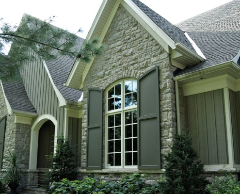 Custom home with green shutters, arched entry and stone siding.