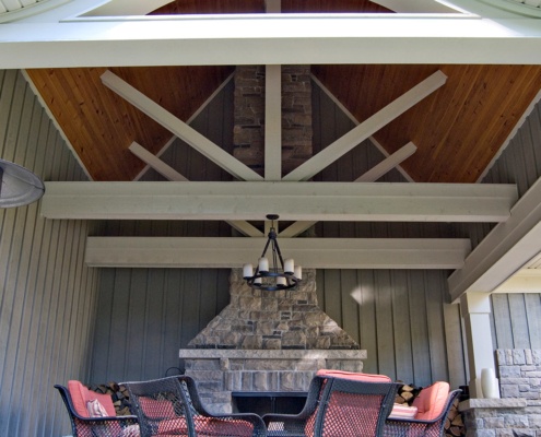 Outdoor deck with stone fireplace, wood siding and wood beams.