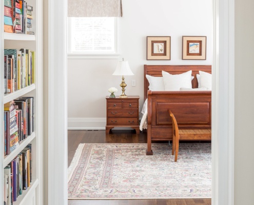 Master bedroom with floor to ceiling bookshelf, wood floor and wood baseboard.