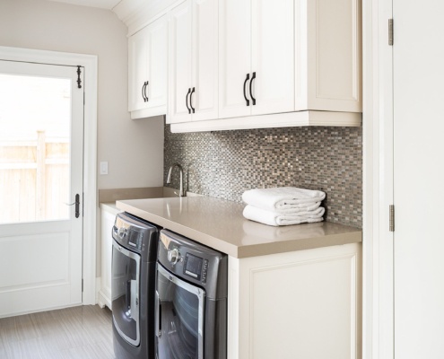 Laundry room with tile floor, tile backsplash and white cabinets.