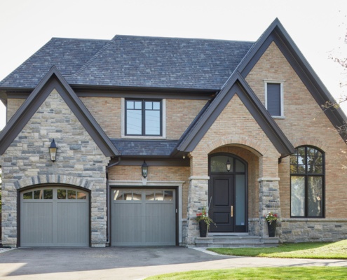 Brick house with dark trim, stone skirt and gray garage door.