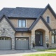 Brick house with dark trim, stone skirt and gray garage door.