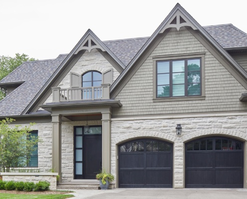 Traditional home with natural stone, black garage door and wood siding.