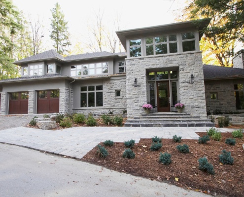 Modern house with stone siding, wood front door and floating roof.