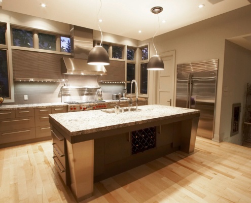 Modern kitchen with granite island, range hood and stainless steel appliances.