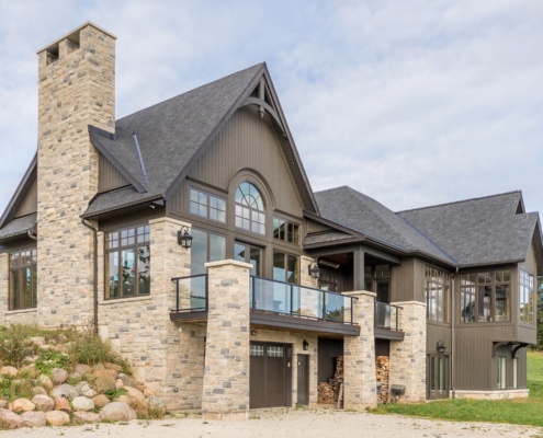 Custom home with second floor balcony, wood storage and glass railing.