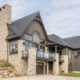 Custom home with second floor balcony, wood storage and glass railing.