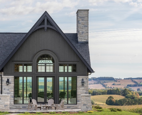 Glass sitting room with stone chimney, wood siding and large windows.