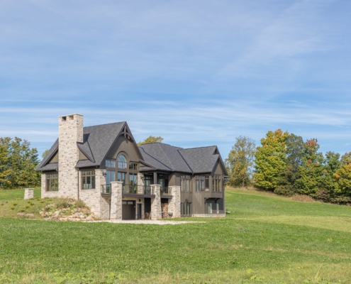 Craftsman style house with stone chimney, angled walls and floor to ceiling windows.