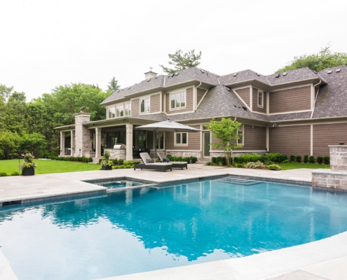 Home backyard with inground pool, wood siding and white trim.