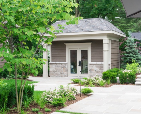 Pool house with stone siding, gray siding and stucco columns.