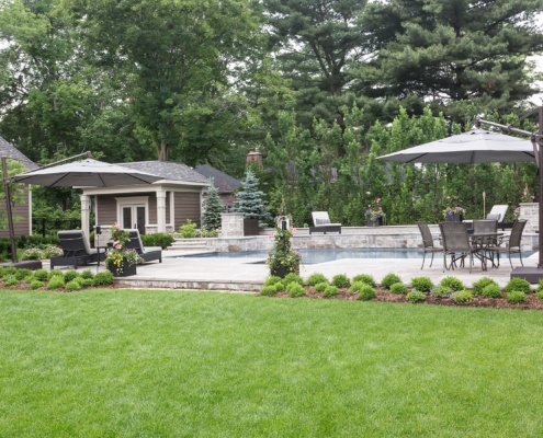 Outdoor flagstone patio with inground pool, pool cabana with wood siding.